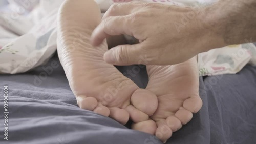 Tickling a sleeping person's feet with a long feather, then with fingers, prompting a startled reaction in their sleep. Funny innocent prank. Close-up shot from the front.
