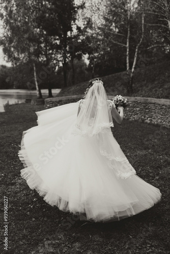 A woman in a wedding dress is walking through a field. She is holding a bouquet of flowers and a veil. The image has a romantic and peaceful mood