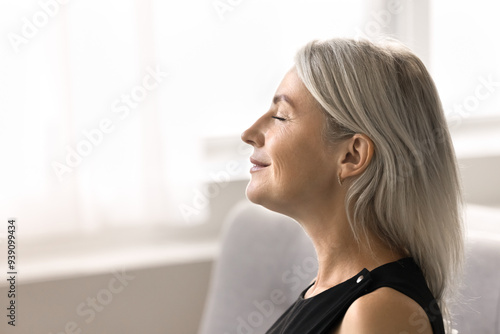 Side profile of serene mature woman breathing fresh conditioned air inside, close up view. Female close her eyes taking moment to relax and unwind, finding peace, boost inner tranquillity. Mindfulness