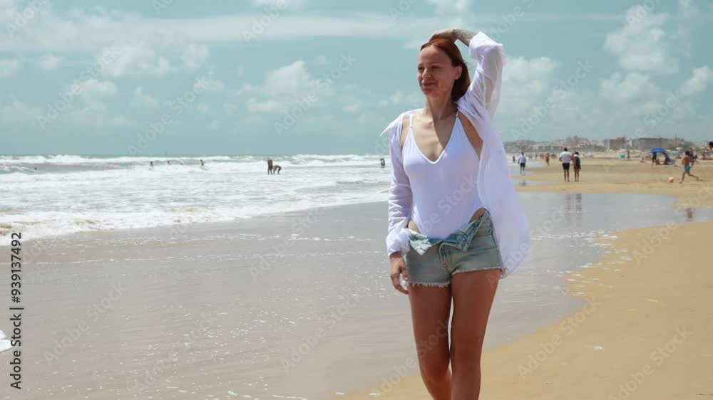 Woman joyfully walks along beach, enjoying sun and gentle breeze while touching her hair Woman joyfully walks along beach, enjoying sun and gentle breeze while touching her hair
