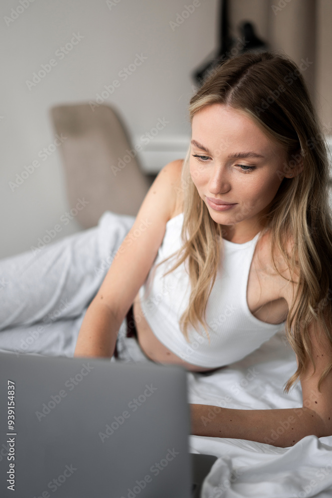 Girl in white top working or watching movie on bed at home using laptop browsing social networks and websites Girl in white top working or watching movie on bed at home using laptop browsing social networks and websites