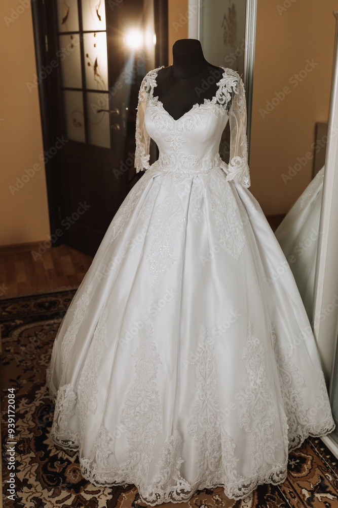 A long white dress with lace and a long train is displayed in a room. The dress is hanging on a mannequin and is the center of attention A long white dress with lace and a long train is displayed in a room. The dress is hanging on a mannequin and is the center of attention