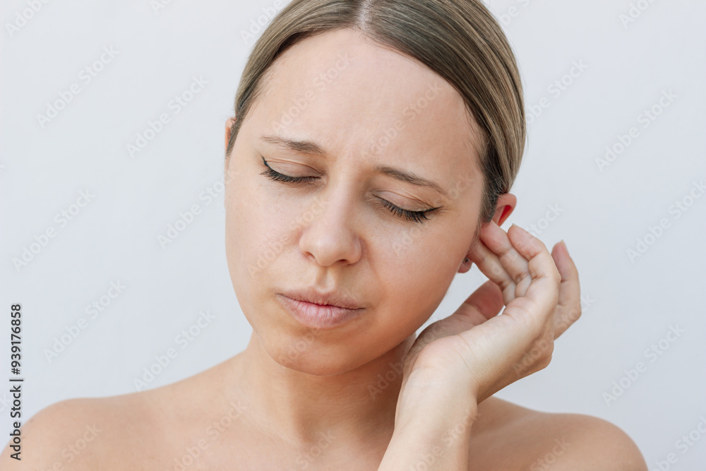 Young caucasian woman pressing on the ear trying to get rid of congestion on a light background. The problem of sulfur plugs. The girl suffering from ear pain Young caucasian woman pressing on the ear trying to get rid of congestion on a light background. The problem of sulfur plugs. The girl suffering from ear pain