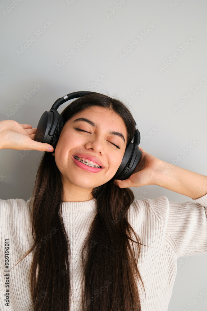 Female smiling teenager with braces listening to music with headphones.