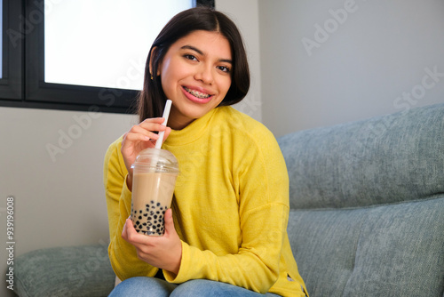 Happy female teenager with braces and a bubble tea sitting in a sofa at home.