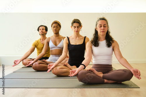 A group of people are sitting on yoga mats and meditating. Scene is peaceful and serene, as the people are meditating and focusing on their breathing.