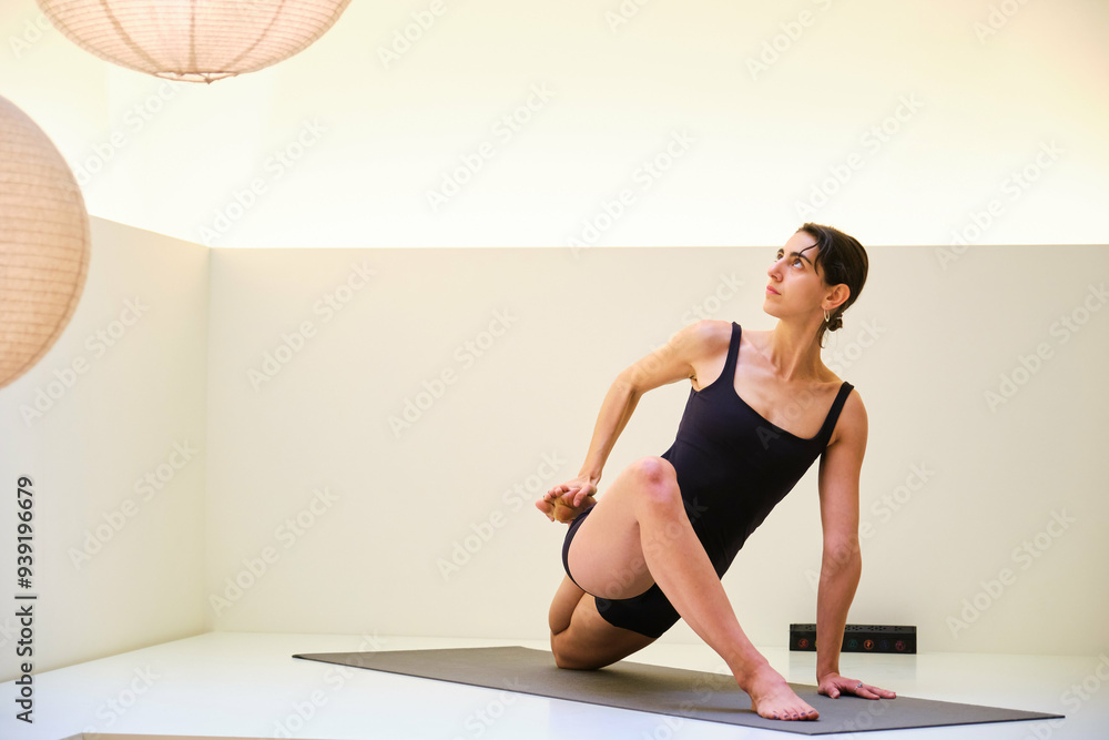 A woman is doing yoga in a studio with a white wall. The room is dimly lit and has a peaceful atmosphere. A woman is doing yoga in a studio with a white wall. The room is dimly lit and has a peaceful atmosphere.