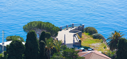 Aerial panoramic view of Belvedere di Via Pirandello in Taormina, Sicily, surrounded by lush greenery with blue Mediterranean sea in background. Serene and picturesque coastal landmark photo