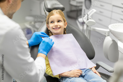 Dentist preparing to conduct teeth-polishing procedure or checkup to little female patient, girl looking at doctor and smiling