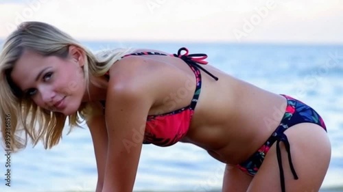 Woman in a bikini bending over at the beach, with the ocean in the background.