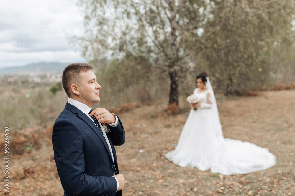 A man in a blue suit is getting ready for his wedding. A woman in a white dress is standing behind him A man in a blue suit is getting ready for his wedding. A woman in a white dress is standing behind him