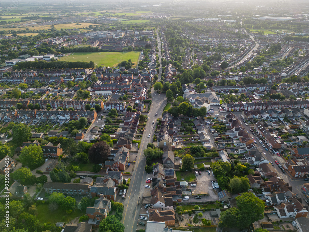 Road and small roundabout in Swindon town UK at sunset in the summer. Aerial view with sun glare. Residential area and school with sport grounds.