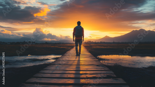 Silhouetted man standing on wooden pier overlooking tranquil lake at sunset with dramatic orange sky and mountain landscape, copy space