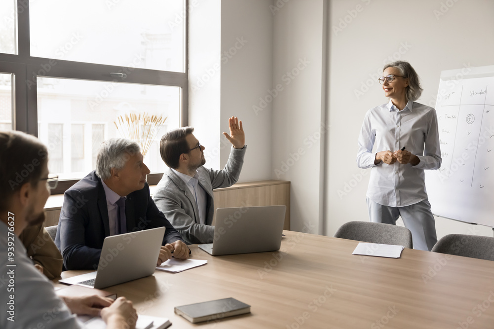 Group of businesspeople take part in educational seminar led by pretty mature female, male participant raising his hand, ask question or make comment, engaged in interactive, collaborative discussion Group of businesspeople take part in educational seminar led by pretty mature female, male participant raising his hand, ask question or make comment, engaged in interactive, collaborative discussion
