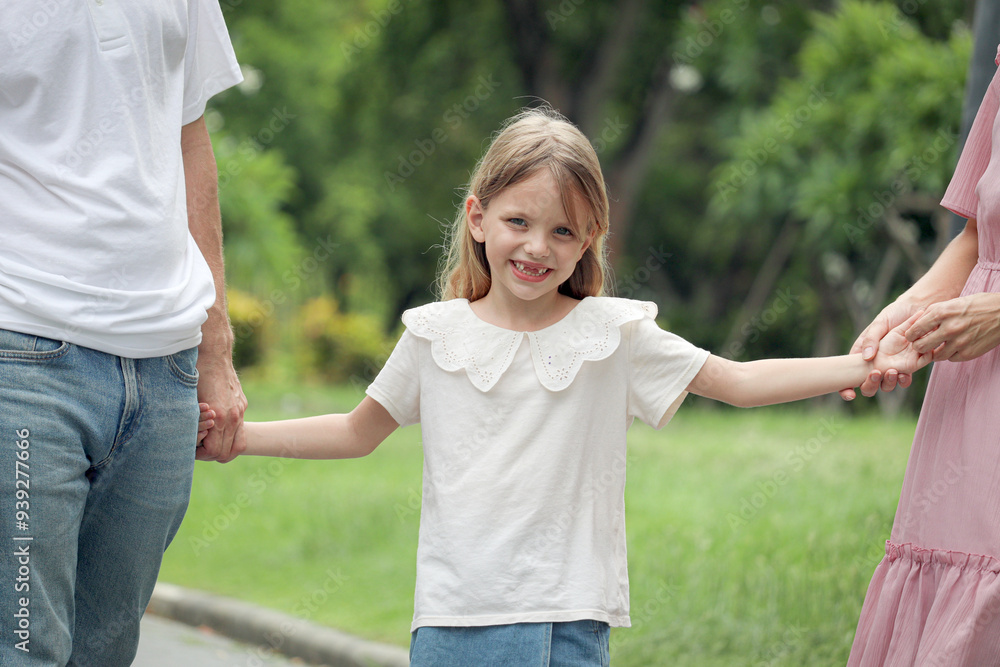 Cute little daughter girl holding father and mother hands taking a walk in beautiful summer garden. Joyful kid spends time together with parents at green park. Smiling child with happy family outside. Cute little daughter girl holding father and mother hands taking a walk in beautiful summer garden. Joyful kid spends time together with parents at green park. Smiling child with happy family outside.