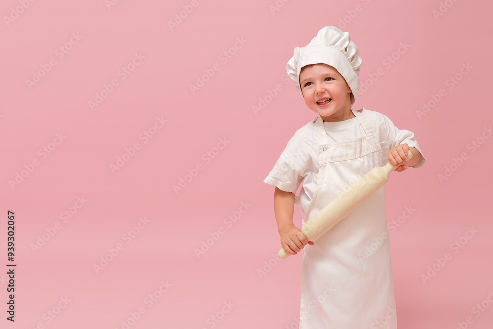 A young child in a chef's outfit is holding a rolling pin. Studio portrait on pink background. Kid aged 3 years (three year old boy) A young child in a chef's outfit is holding a rolling pin. Studio portrait on pink background. Kid aged 3 years (three year old boy)