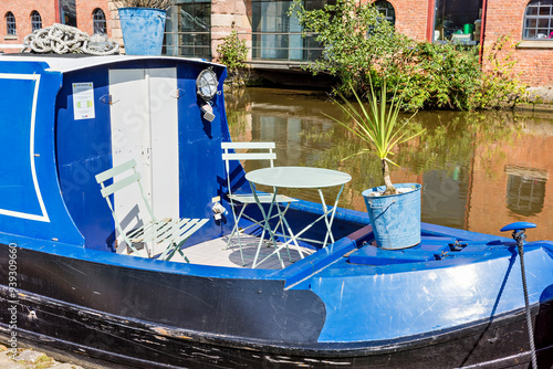 Blue canal boat with a small seating area and potted plants on a calm river. photo