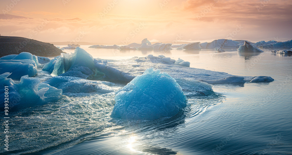 Sun setting over a serene glacial ice lagoon. Blue icebergs floating in water waves. Ice Lagoon, Iceland, Northern Europe.