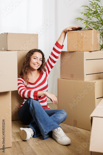 Young woman in her new house surrounded by cardboard boxes, they reach the ceiling. Happy, smiling and excited young girl opening moving boxes in student rental apartment. photo