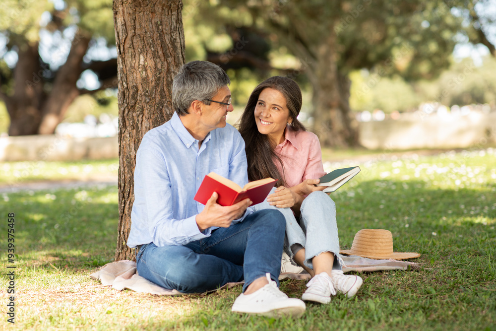 A couple enjoys a quiet afternoon under a tree, sharing their favorite books. The sun shines brightly as they smile and engage in conversation, surrounded by greenery. A couple enjoys a quiet afternoon under a tree, sharing their favorite books. The sun shines brightly as they smile and engage in conversation, surrounded by greenery.