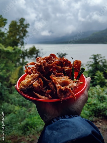 Holding Indian street food kanda bhaji dish having nature scenery in background, favourite Indian snack in monsoon , India