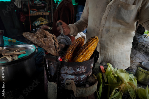Seller man making roasted grilled corn in streets in rainy season, India