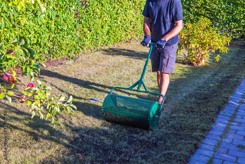 Foto Man restoring lawn using soil spreader roller on grass in garden