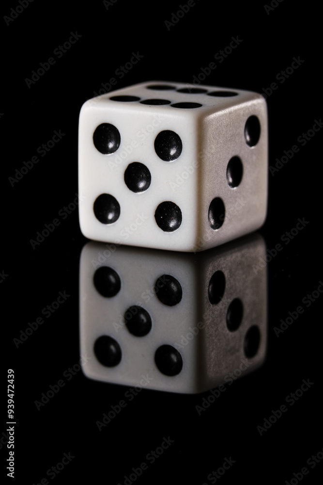 a white six-sided D6 dice with black dots, showing five dots, on a black background with a reflection a white six-sided D6 dice with black dots, showing five dots, on a black background with a reflection