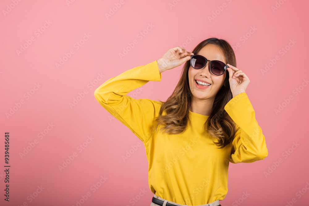 Portrait Asian woman in a yellow shirt is smiling and holding up her sunglasses studio shot isolated on pink background. Concept of happiness and carefree attitude, Thai female Portrait Asian woman in a yellow shirt is smiling and holding up her sunglasses studio shot isolated on pink background. Concept of happiness and carefree attitude, Thai female