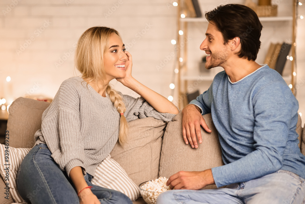 Cozy evening. Loving couple talking and eating popcorn in living room, free space Cozy evening. Loving couple talking and eating popcorn in living room, free space