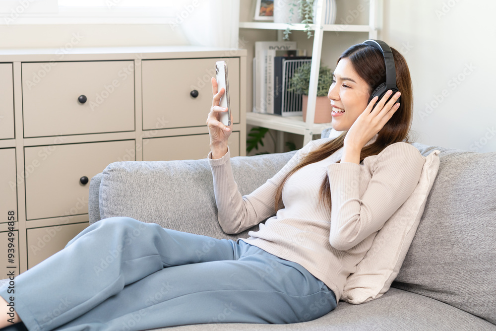 Relaxing concept asian young woman, girl using smart phone listening to music, enjoy song or watching app online social with wireless headphones lying on sofa or couch, chill out and leisure at home. Relaxing concept asian young woman, girl using smart phone listening to music, enjoy song or watching app online social with wireless headphones lying on sofa or couch, chill out and leisure at home.