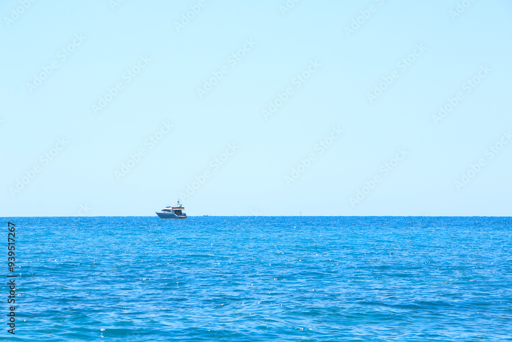 A lone boat floats on the distant horizon of a calm blue sea under a clear sky. The serene water surface gently ripples, creating a peaceful and tranquil ocean scene. A lone boat floats on the distant horizon of a calm blue sea under a clear sky. The serene water surface gently ripples, creating a peaceful and tranquil ocean scene.