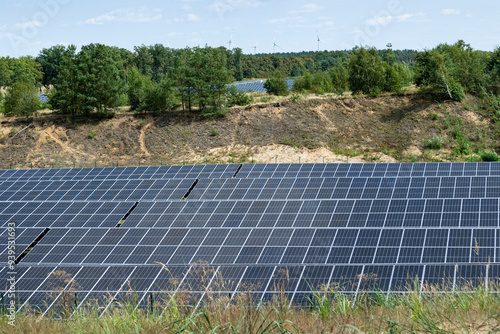 Photovoltaik Freiflächenanlage; ehemalige Kiesgrube am Waldrand; im Hintergrund Windräder eines Windparks photo