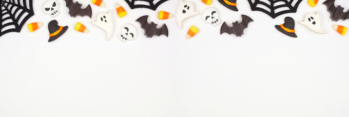 Halloween top border of black, white and orange color candy and spider webs. Overhead view on a white banner background with copy space.