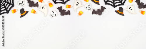 Halloween top border of black, white and orange color candy and spider webs. Overhead view on a white banner background with copy space.