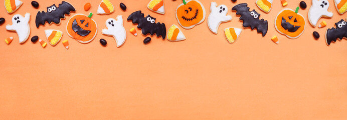 Halloween cookie top border. Overhead view on an orange banner background with copy space. Ghosts, bats, jack o lanterns and candy corn.