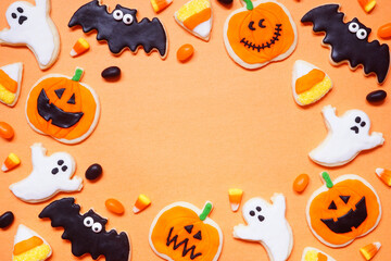 Halloween cookie frame. Top view on an orange background with copy space. Ghosts, bats, jack o lanterns and candy corn.