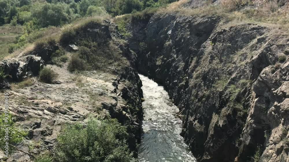 Serene Mountain Stream Flowing Through a Narrow Rocky Gorge in a Lush Green Valley Under a Clear Summer Sky Serene Mountain Stream Flowing Through a Narrow Rocky Gorge in a Lush Green Valley Under a Clear Summer Sky