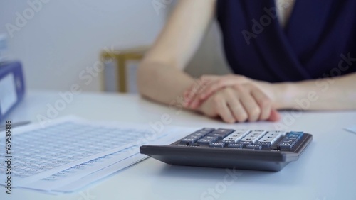 Businesswoman with dark blue dress is sitting at her desk with financial documents and a calculator, waiting for a meeting to begin