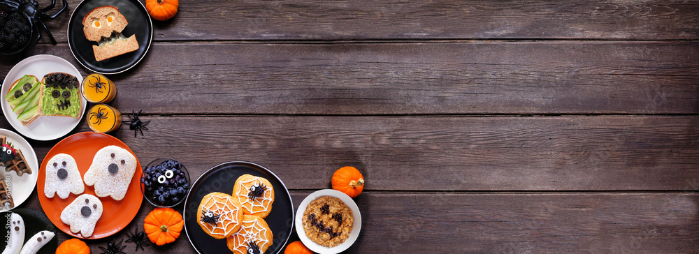 Spooky Halloween breakfast corner border over a dark wood banner background with copy space. Top view. Assorted pancakes, toast, oatmeal and fruit. Spooky Halloween breakfast corner border over a dark wood banner background with copy space. Top view. Assorted pancakes, toast, oatmeal and fruit.