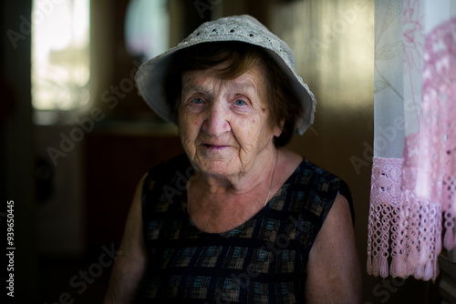 An elderly woman in a sun hat, portrait in her rustic village home.