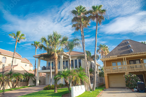 Row of two-story beach house vacation home rental property with porch, clay tile roofs with line of palm trees under sunny cloud blue sky near downtown South Padres Island, travel destinations