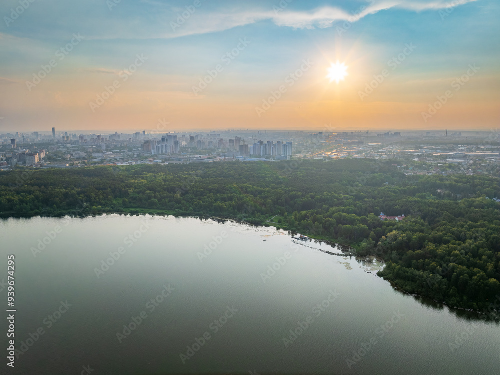 Fototapeta premium Big lake with green shores in bright sun light and city on horizon, aerial landscape. Recreation concept. Aerial view