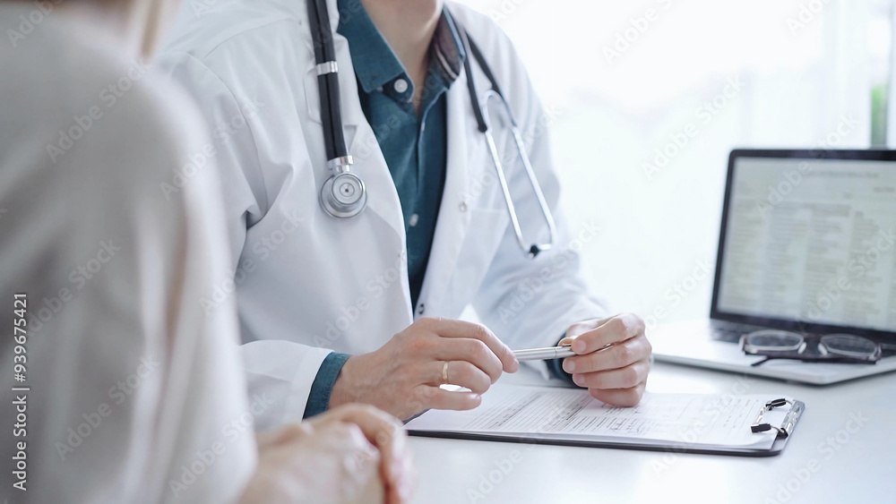 Doctor and a patient. The physician, wearing a white medical coat over a green shirt, is gesturing with his hands during a consultation in the clinic. Medicine Doctor and a patient. The physician, wearing a white medical coat over a green shirt, is gesturing with his hands during a consultation in the clinic. Medicine