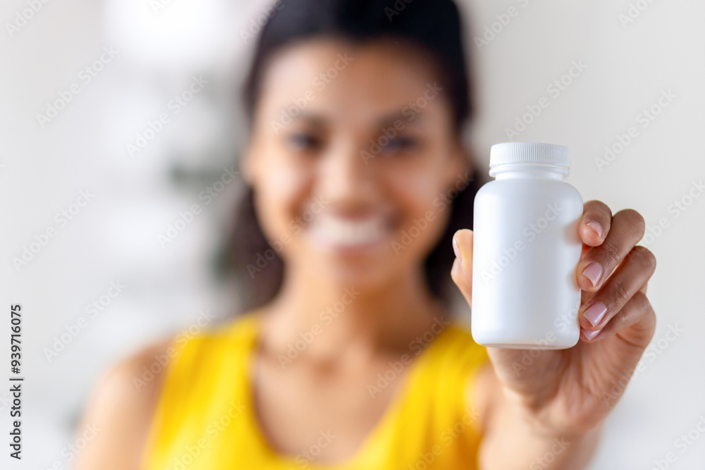 A smiling woman holding a white vitamin bottle, promoting health and wellness. Supplements, healthcare, and a healthy lifestyle concept