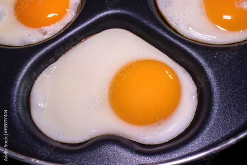 Close-up of fried eggs in a pan, with one egg shaped like a heart, highlighting the health and nutritional properties of eggs. photo