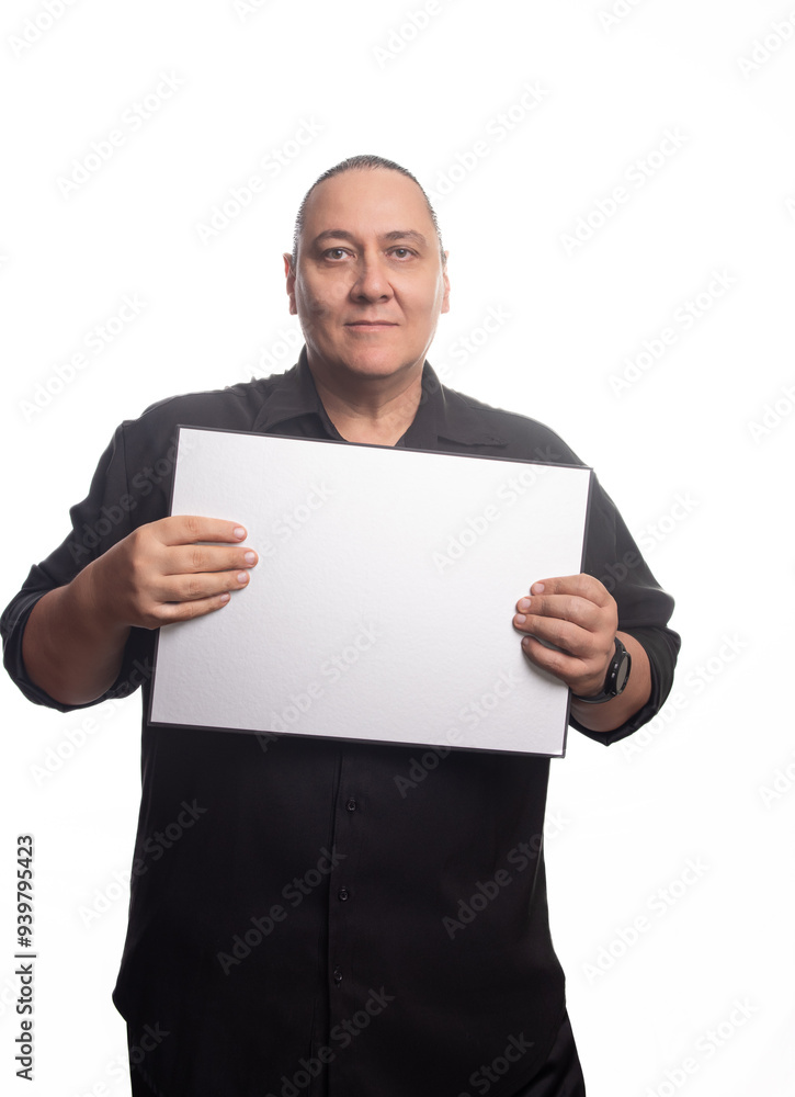 Adult man, an adult man in black clothing holding a blank sign in front of a white background, selective focus. Adult man, an adult man in black clothing holding a blank sign in front of a white background, selective focus.