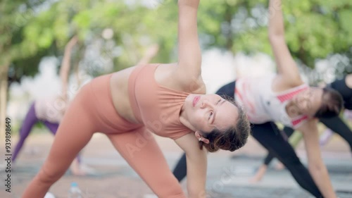 A group of people are doing yoga in a park. The woman in the orange top is doing a pose photo