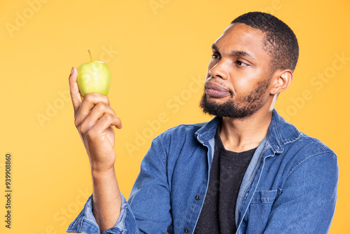 Фототапет African american zero waste enthusiast looks at green apple on camera, enjoying raw healthy nutrition with ethically sourced fresh fruits