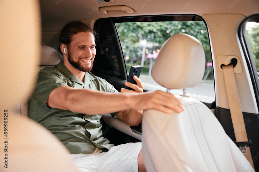 Young man enjoying time in a car, using a smartphone and wearing earbuds, smiling and relaxed Young man enjoying time in a car, using a smartphone and wearing earbuds, smiling and relaxed